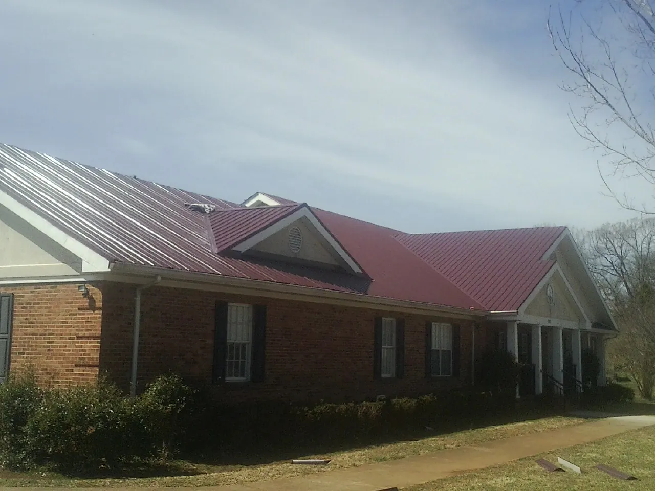 Red metal roof with gabled entries on a long brick building, from a Hail Damage Roof Repair job in Indian Rocks Beach