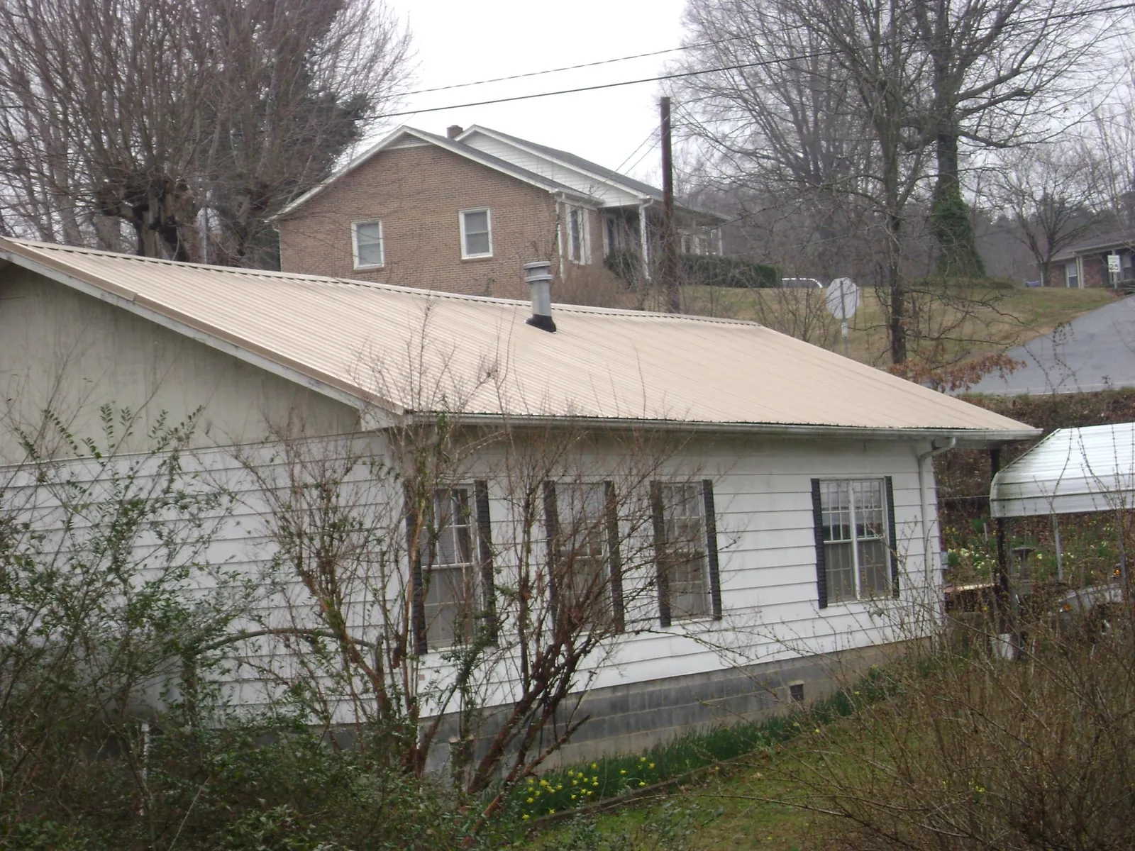 Tan metal roof on a white sided house set into a hillside — Commercial Roofing by Roofing Brothers in Indian Rocks Beach